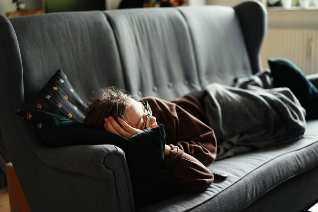 Frau in rosa Jacke auf grauer Couch liegend