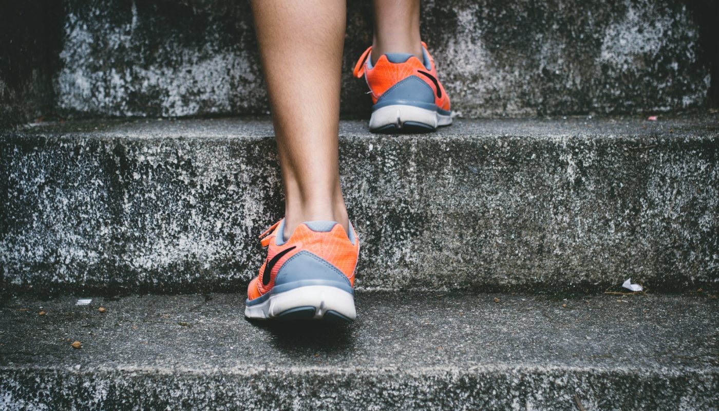 Person mit orangefarbenen und grauen Nike-Schuhen, die auf einer grauen Betontreppe läuft