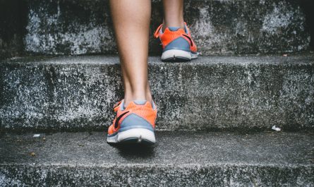 Person mit orangefarbenen und grauen Nike-Schuhen, die auf einer grauen Betontreppe läuft